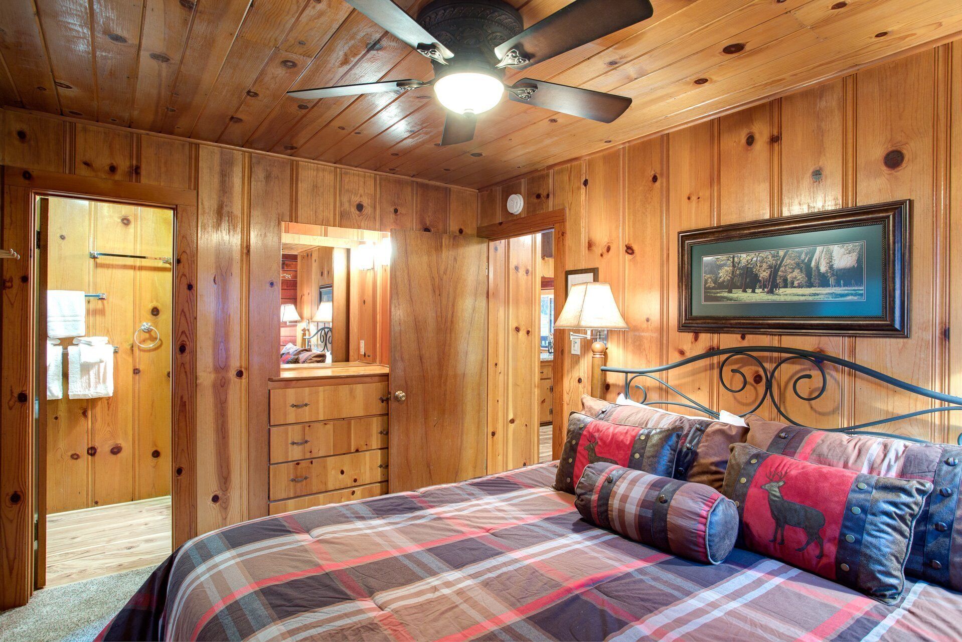 A wooden cabin bedroom with a bed, a ceiling fan, a dresser, and a framed picture on the wall.