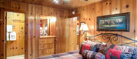 A wooden cabin bedroom with a bed, a ceiling fan, a dresser, and a framed picture on the wall.