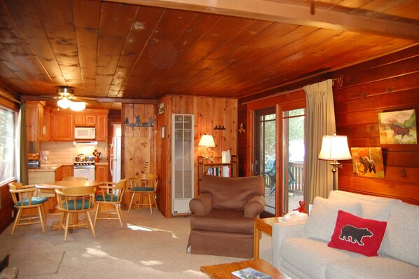 A cabin interior with a dining area, a living room with a sofa and a chair, a fireplace, and a kitchen with a microwave.