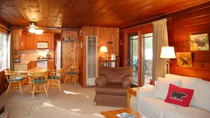 L’intérieur d’un chalet en bois comprend un coin repas, un salon avec un canapé et un fauteuil, ainsi qu’une cuisine dotée de meubles en bois et d’un four à micro-ondes.