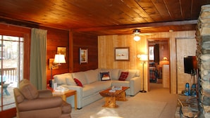 L’intérieur d’un chalet accueillant, avec un plafond en bois, un canapé, une table basse et un téléviseur.