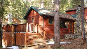 Une cabane en bois avec une cheminée en pierre, une terrasse en bois et un mur en pierre.
