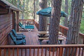A wooden deck with lounge chairs and picnic tables, surrounded by large trees.