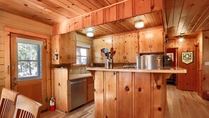 A wooden cabin interior with a kitchen area, including a wooden island, cabinets, and a fire extinguisher. - Walk-a-bout (Yosemite National Park)