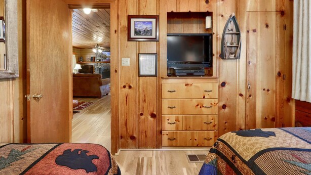 A wooden-paneled room with a television, a fireplace, and a bed with a quilt.