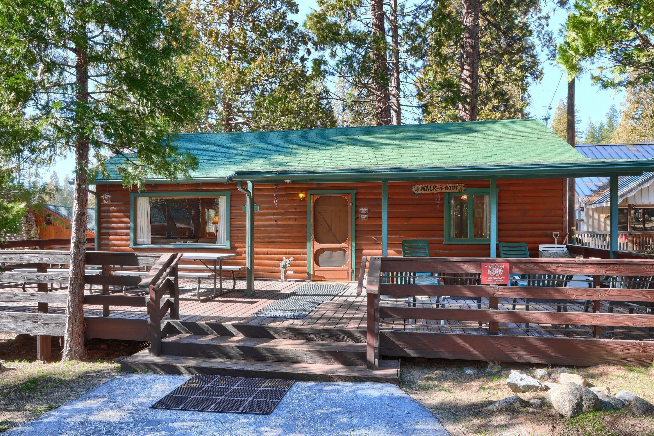 A rustic log cabin with a green roof, a covered porch, and a sign reading "Walk-in BOUT."