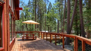 A wooden deck with a picnic table and umbrella, surrounded by tall trees. - Jolie Cabin (Yosemite National Park)