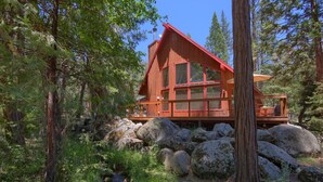 A rustic cabin with a red roof and large windows, surrounded by a forest and large rocks. - Jolie Cabin (Yosemite National Park)