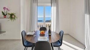 Un coin repas avec une table dressée pour deux personnes, une vue sur la mer et un balcon agrémenté de plantes en pot.