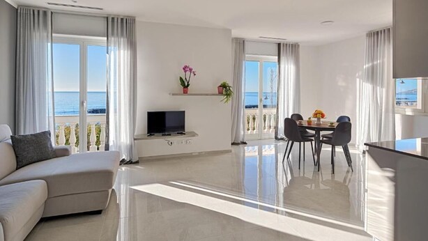 Un salon moderne comprenant un canapé, une table à manger avec des chaises, un téléviseur et un balcon avec vue sur la mer.