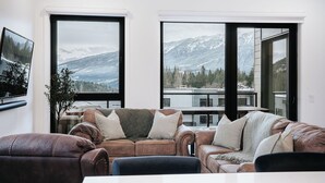A modern living room with a large window overlooking a snowy mountain landscape. - Cloudscape PenthouseRevelstoke Vacations (Revelstoke)