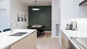 A modern kitchen with a white countertop, stainless steel sink, and a dining area with a table and chairs. - Cloudscape PenthouseRevelstoke Vacations (Revelstoke)