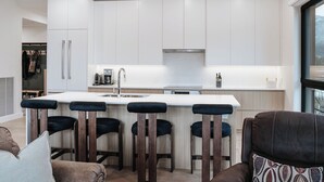 A modern kitchen with white cabinets, a central island with bar stools, and a large window. - Cloudscape PenthouseRevelstoke Vacations (Revelstoke)