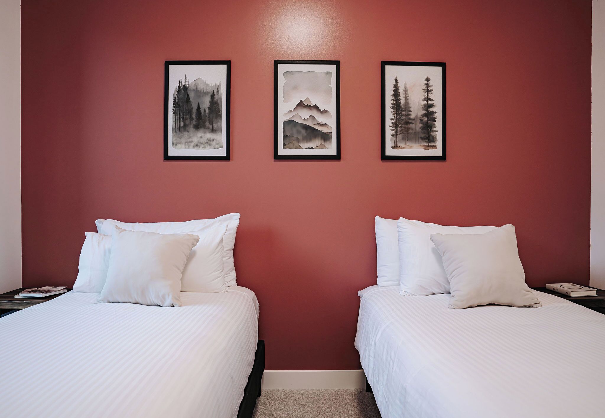 Ein Hotelzimmer mit zwei Betten, einer roten Wand und drei gerahmten Bildern von Bergen und Bäumen.