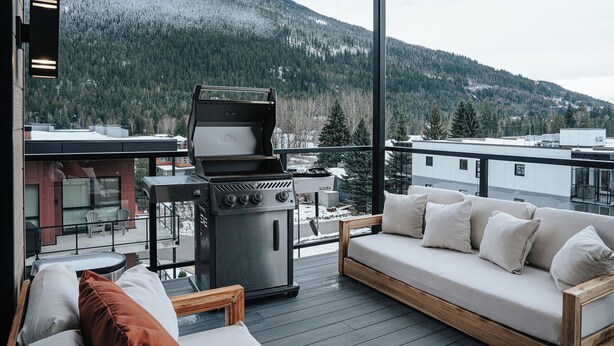 Un balcon avec un barbecue, un canapé et une vue sur une montagne enneigée.