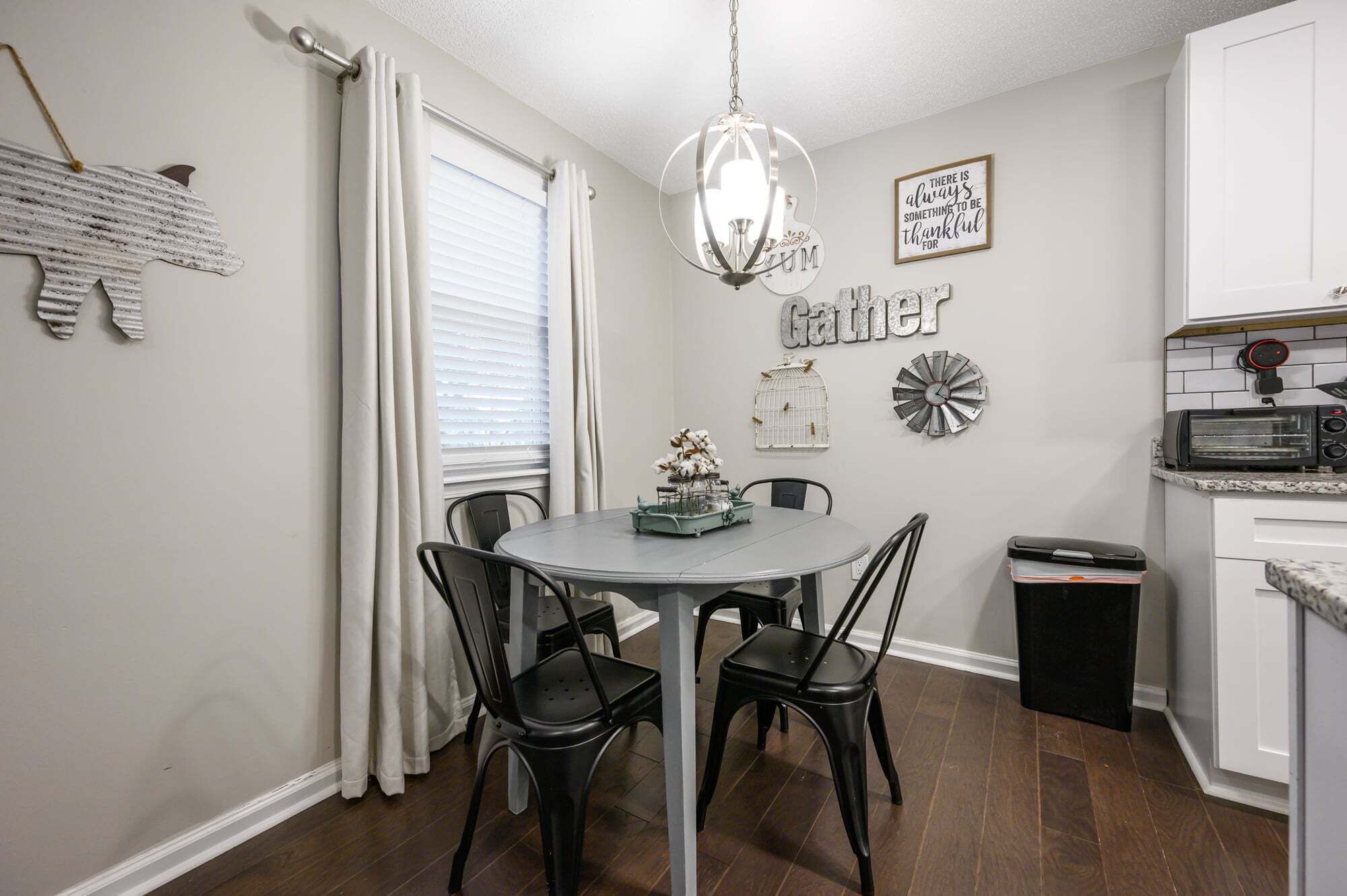 A dining area with a round table, black chairs, a chandelier, and wall decorations including a birdcage and a clock.