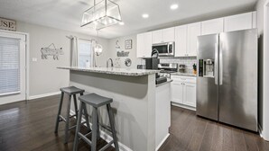A modern kitchen with white cabinets, a stainless steel refrigerator, a built-in microwave, and a central island with stools. - 10 Jill Lane, Cartersville (Cartersville)