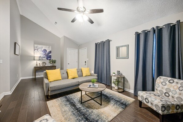 A living room with a gray sofa, yellow pillows, a round coffee table, and a patterned armchair. - 10 Jill Lane, Cartersville (Cartersville)