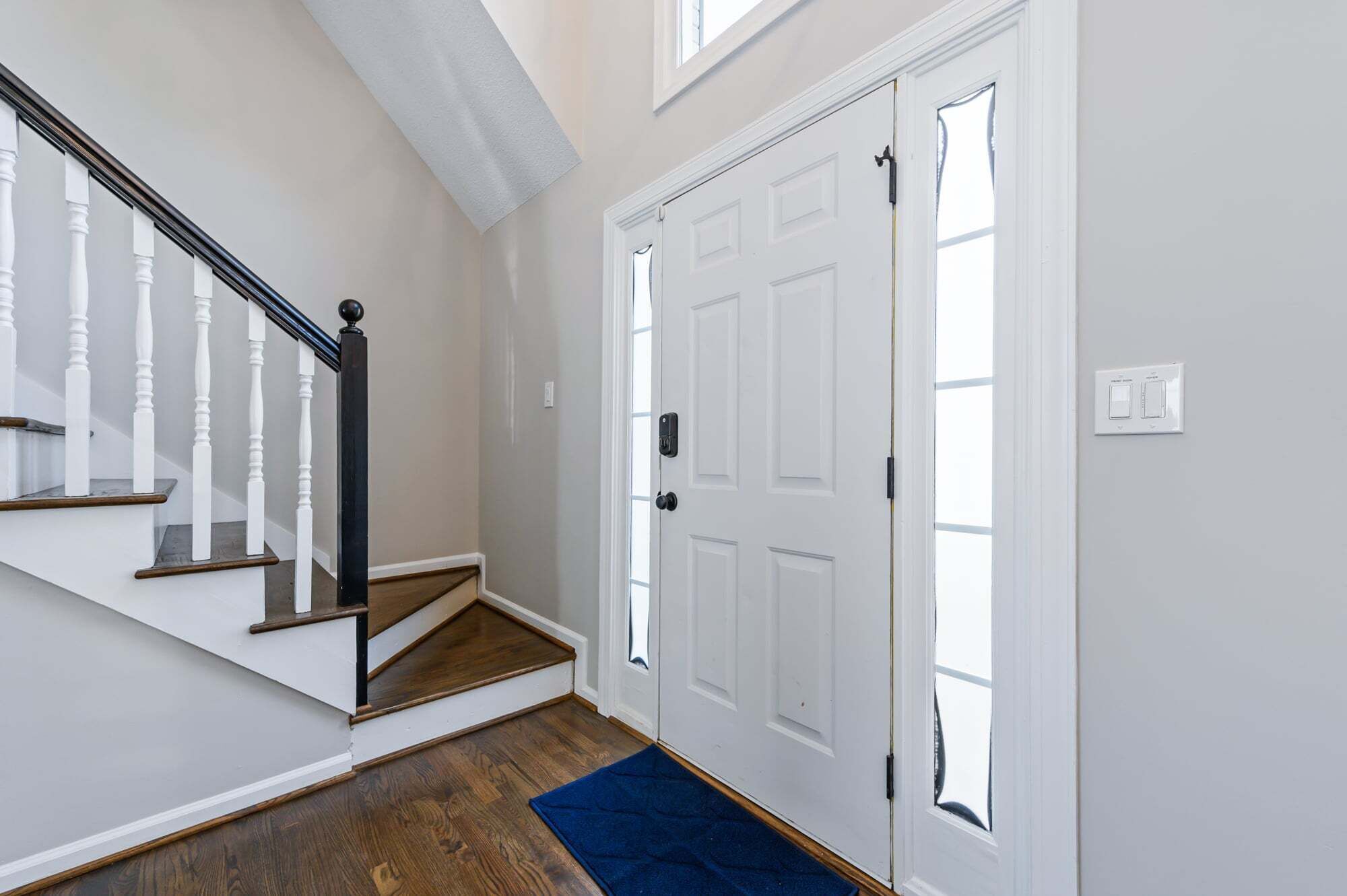 Un escalier avec des balustrades blanches et une main courante sombre, menant à une porte blanche ornée d’une petite fenêtre.