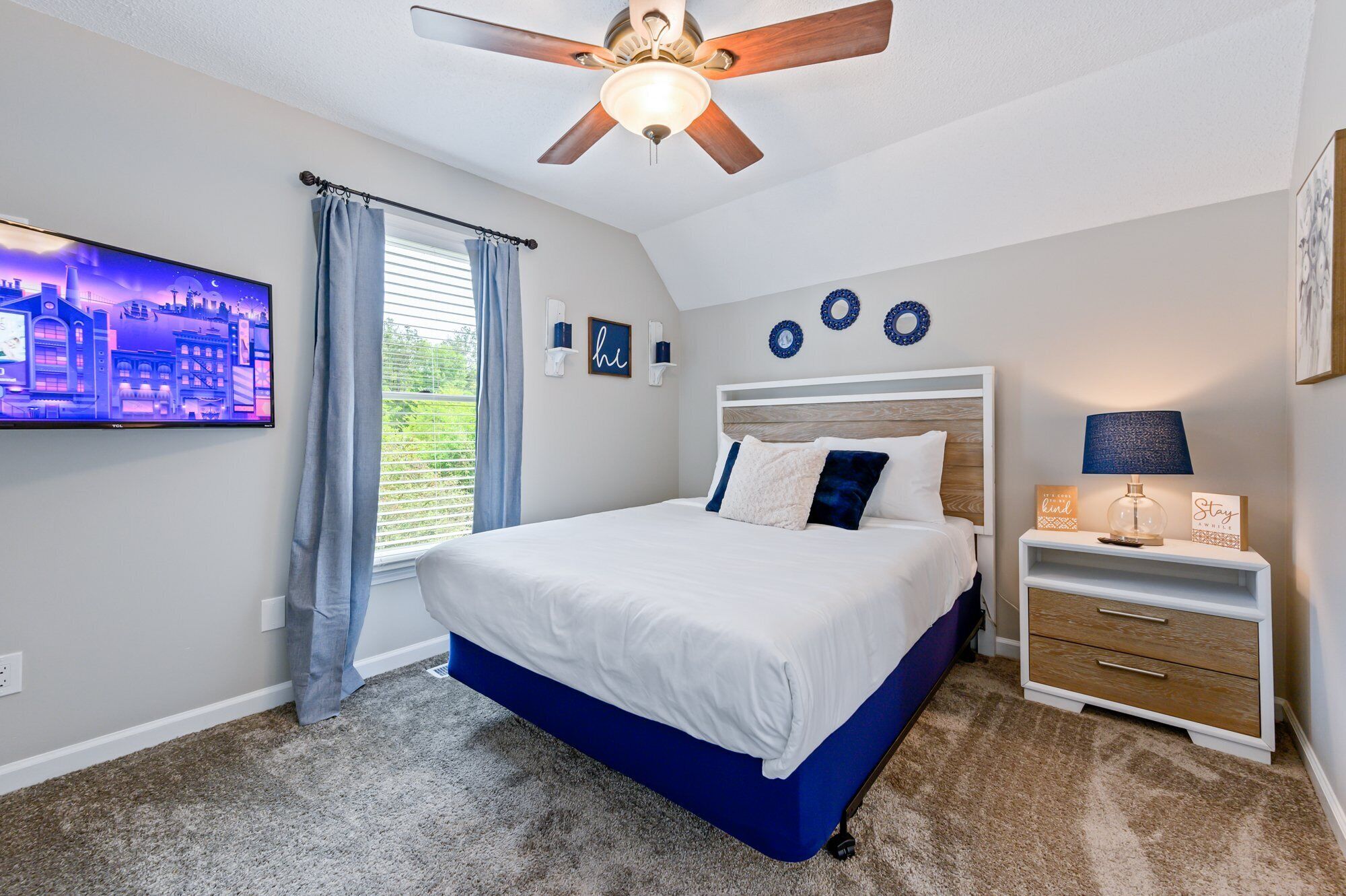 A bedroom with a bed, a ceiling fan, a TV, a nightstand, and decorative wall plates.