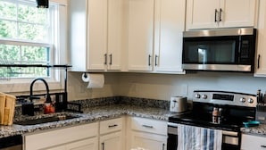 A modern kitchen with white cabinets, a granite countertop, stainless steel appliances, and pendant lighting.