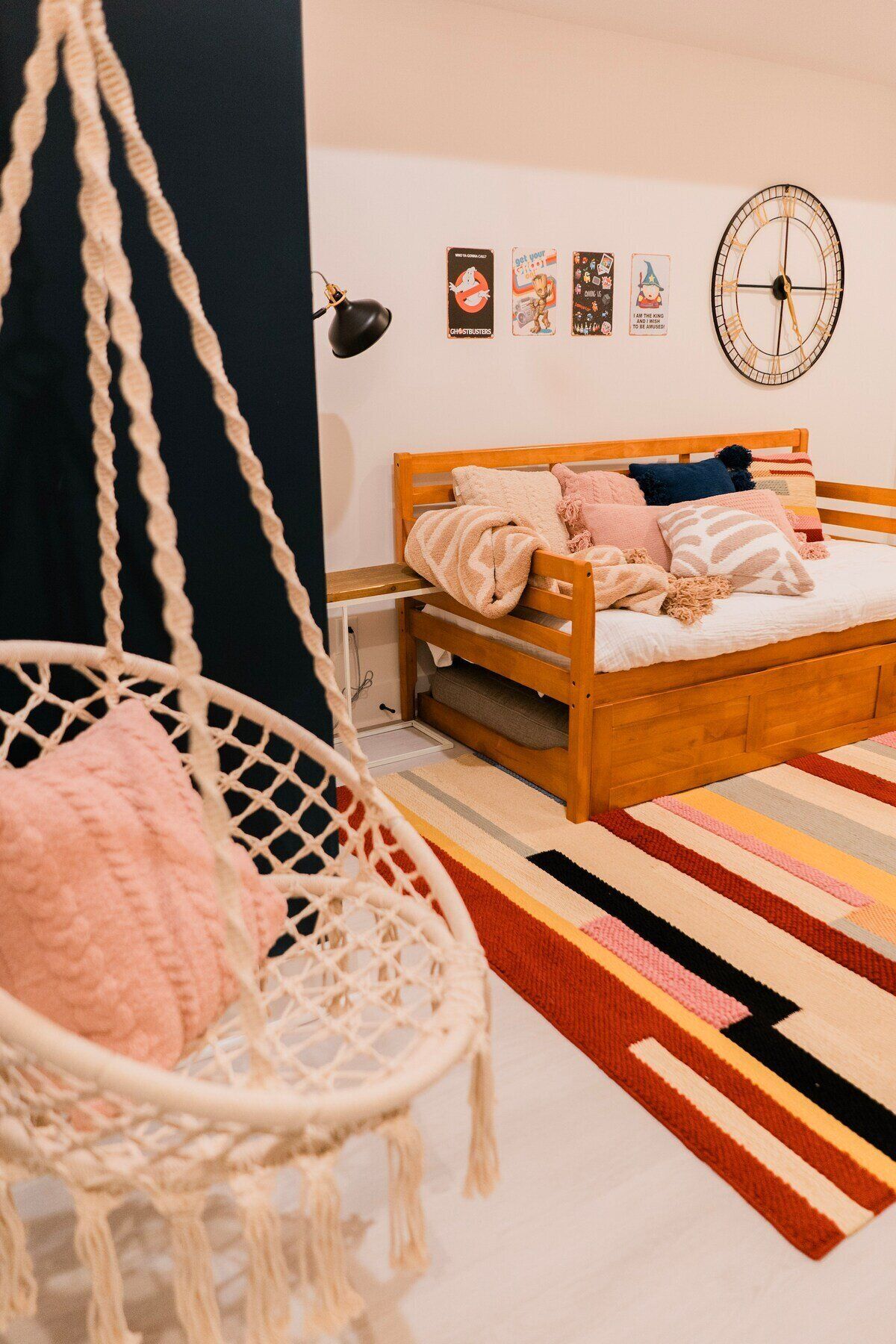 A bedroom with a wooden bed, a hanging chair, a wall clock, and a striped rug.