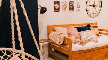 A bedroom with a wooden bed, a hanging chair, a wall clock, and a striped rug.