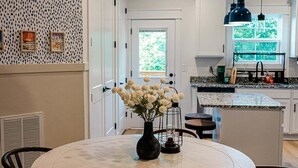 A modern kitchen with a round dining table, pendant lighting, and a view to the outdoors.