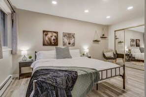 A bedroom with a bed, bedside tables, a mirror, and wall art. - 4925 Pike Unit2 (Cascade)