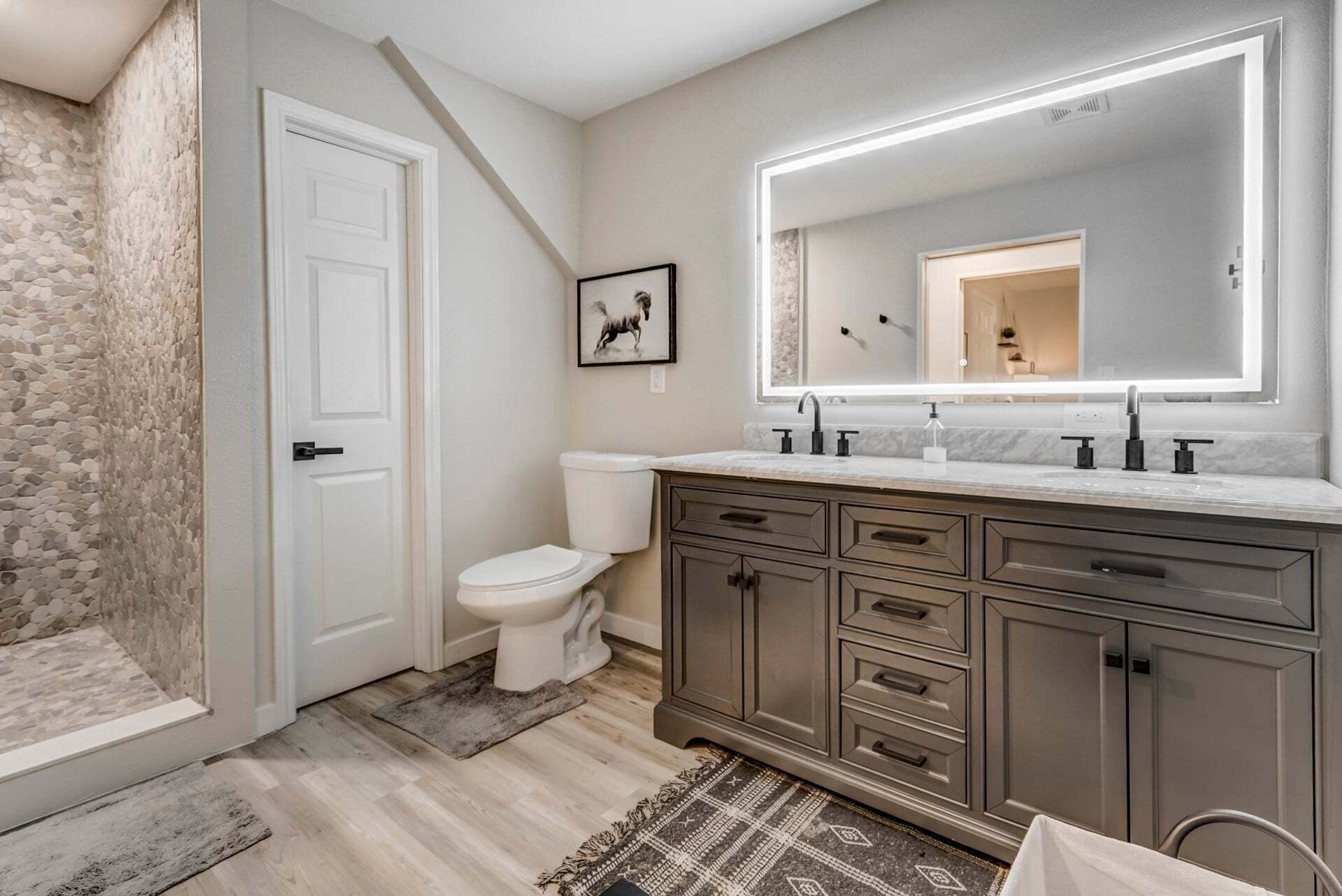 A bathroom with a white toilet, a large mirror, a marble countertop, and a stone wall.