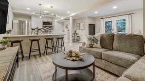 A modern living room with a sofa, a round coffee table, and a kitchen area with a refrigerator, microwave, and bar stools. - 4925 Pike Unit2 (Cascade)