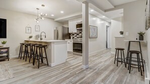 A modern kitchen with a central island, bar stools, and a dining area with a high table. - 4925 Pike Unit2 (Cascade)