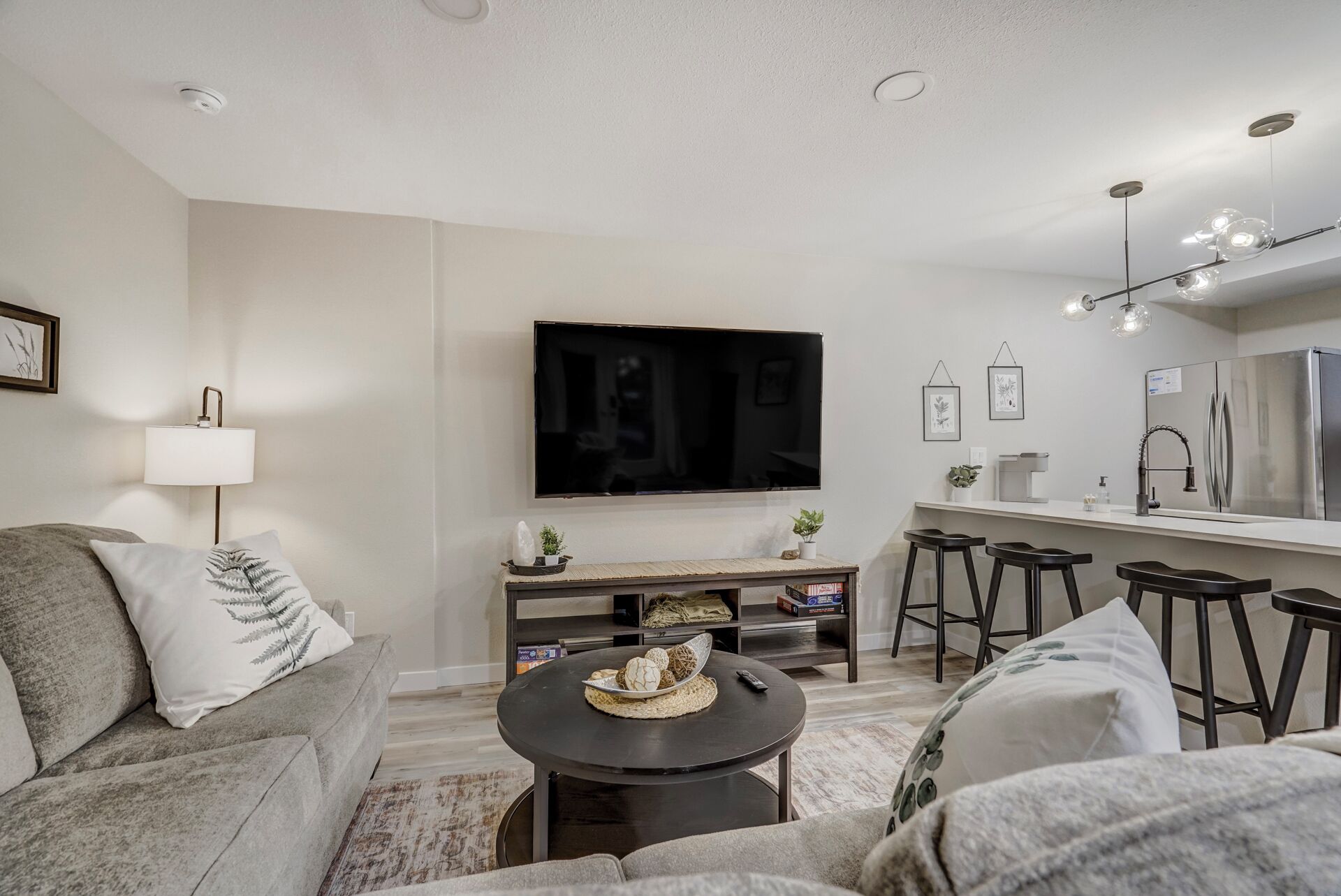 A modern living room with a sofa, a round coffee table, a TV, and a kitchen area with stools.