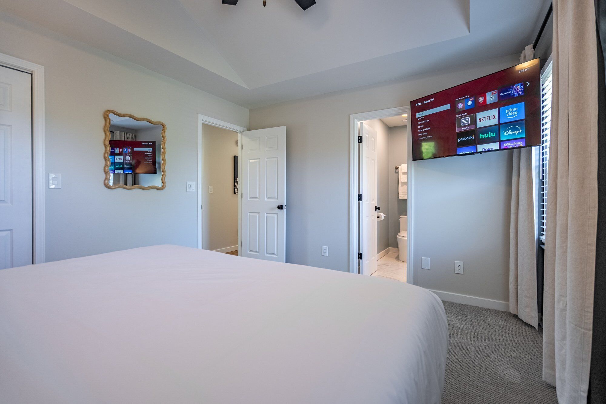 Habitación de hotel con una cama grande, un televisor en la pared que muestra servicios de streaming y una puerta que da a un baño.