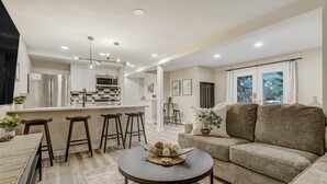 A modern living room with a sofa, a round coffee table, and a kitchen area with a refrigerator, microwave, and bar stools. - 4925 Pike (Cascade)