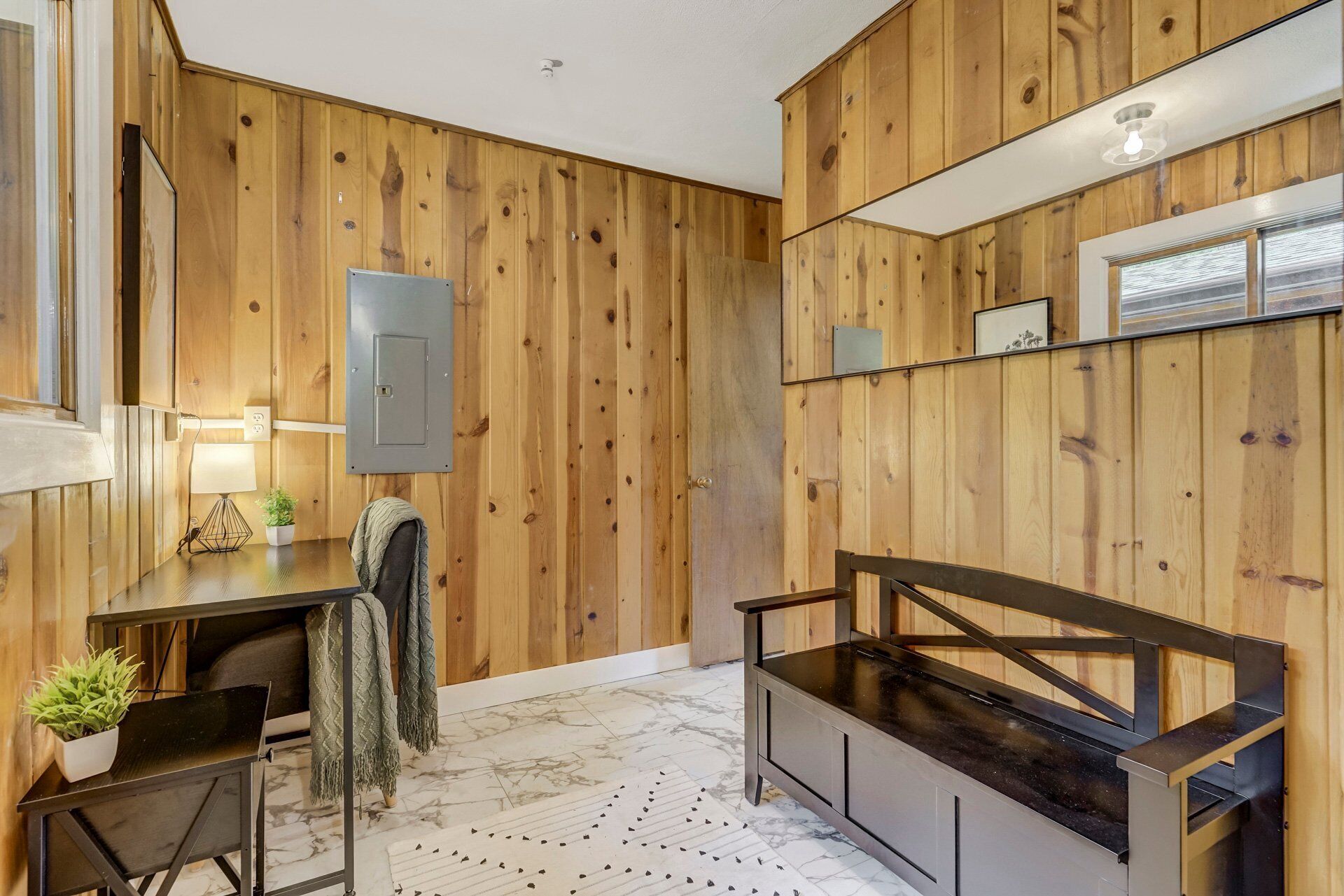A modern bathroom with wooden paneling, a black vanity, a mirror, and a small table with a lamp and plant.