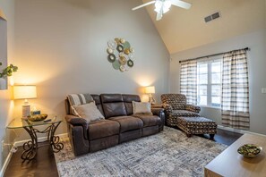 A living room with a brown leather sofa, patterned armchair, and a decorative wall piece. - 106 Middlebrook Dr, Cartersville (Cartersville)
