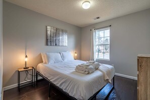 A bedroom with a bed, bedside lamps, a window, and a painting on the wall. - 106 Middlebrook Dr, Cartersville (Cartersville)