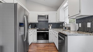 Une cuisine moderne dotée d’appareils électroménagers en acier inoxydable, de meubles blancs, d’un dosseret en carreaux disposés en motif chevrons et d’un plancher en bois.