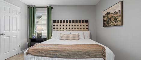 A bedroom with a bed, a headboard, a nightstand, a lamp, a door, and a painting on the wall.