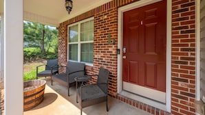 A brick house with a red door, a covered porch with wicker furniture, and a large window. - 18 Larkspur Ln Emerson (Emerson)
