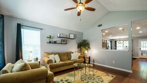 A living room with a sofa, a coffee table, a patterned rug, a ceiling fan, and a wall-mounted shelf with decorative items. - 18 Larkspur Ln Emerson (Emerson)