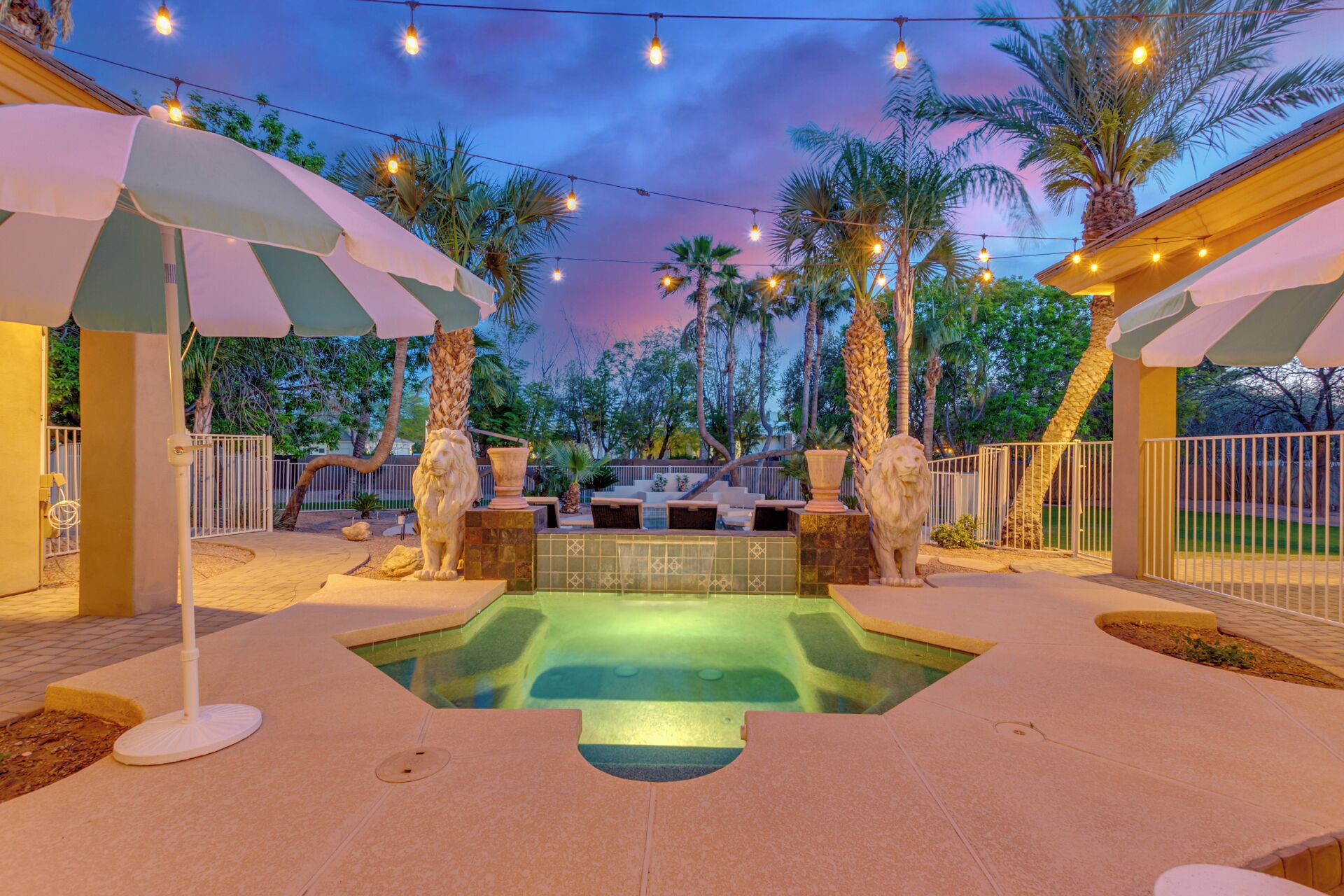 A pool area with two stone lion statues, surrounded by palm trees and string lights.