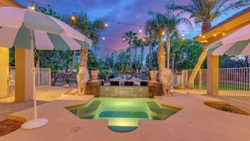 A pool area with two stone lion statues, surrounded by palm trees and string lights.