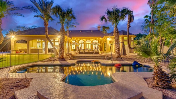 Una lussuosa casa con piscina, palme e un patio ben illuminato.