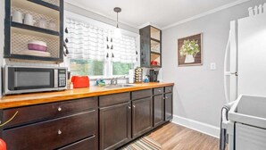 A kitchen with dark wooden cabinets, a microwave, a sink, and a window with curtains. - 1BD 102 Madison Ter (Clarksville)