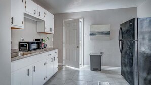 Una cocina con armarios blancos, un refrigerador negro, un microondas y un lavamanos.