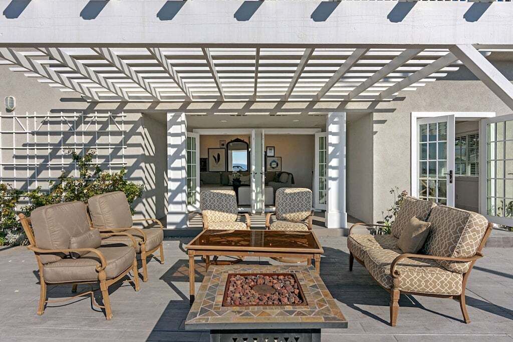 Ein Garten-Terrasse mit Korbmöbeln, einem Glastisch und einem Feuerkorb.