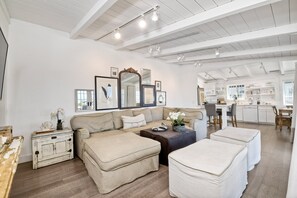 Ein geräumiger Wohnbereich mit einem beigefarbenen Sofa, Poufs, einem Couchtisch und einem weißen Schrank.