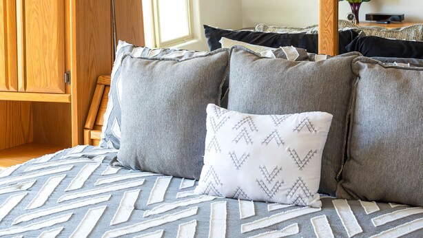 Una cama bien hecha con una colcha estampada, una lámpara de noche y un cabecero de madera.
